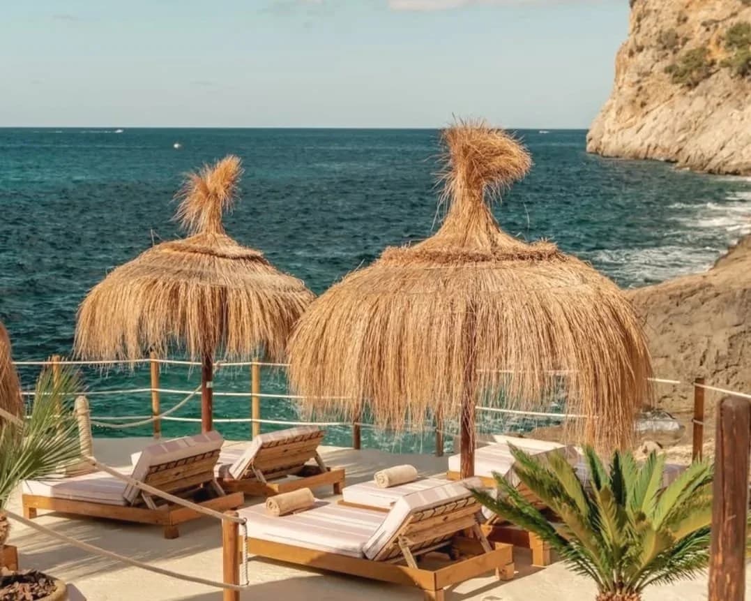 Beach scene with straw umbrellas, wooden lounge chairs, and the ocean in the background.